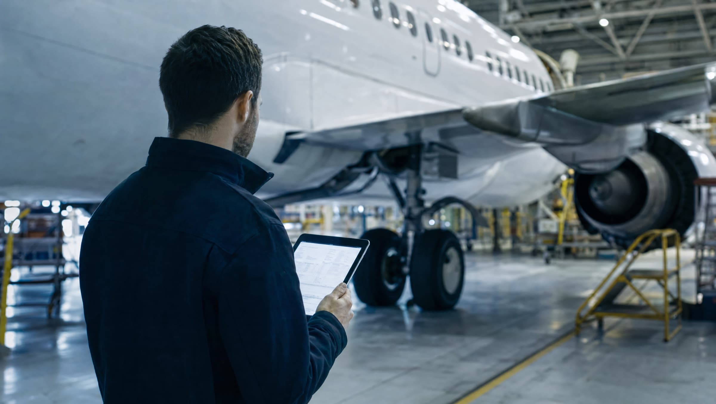 Engineer reviewing airworthiness records on a tablet beside an aircraft in a hangar